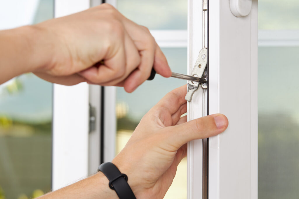handyman adjusting white pvc plastic window indoors. worker using screwdriver to repair upvc window. homework maintenance.